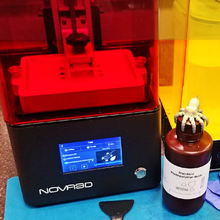A 3D printer next to a bottle of photopolymer resin with a small octopus model on top.