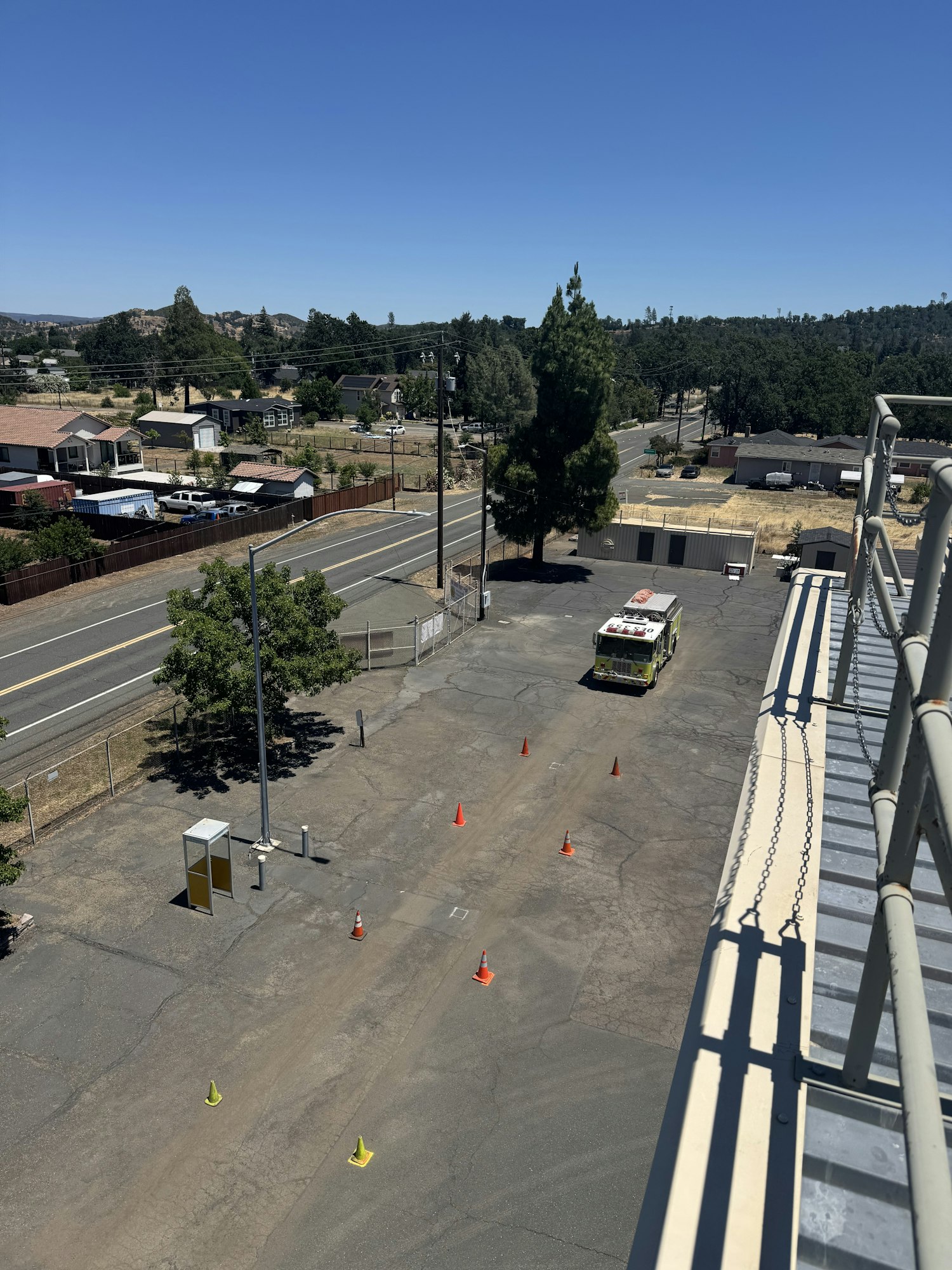 An aerial view of a road with traffic cones, an emergency vehicle, and nearby buildings under a clear blue sky.