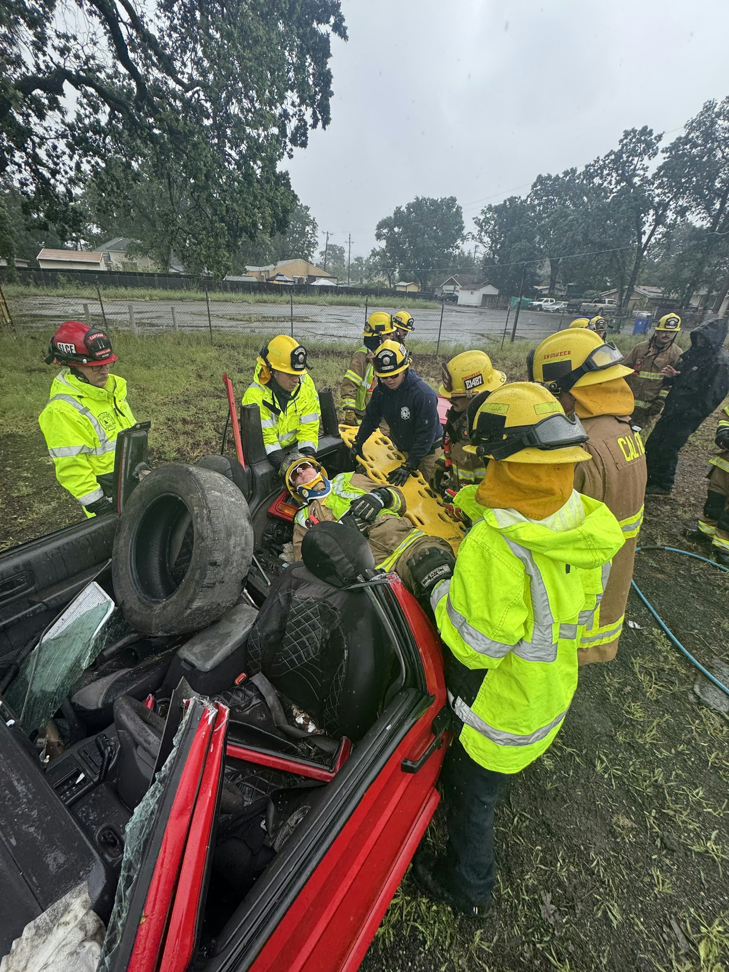 Emergency responders, including firefighters, work on a scene involving an overturned car, attending to potential victims.