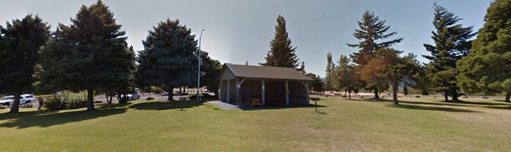 A park scene with a pavilion, surrounded by trees and grass under a clear sky.
