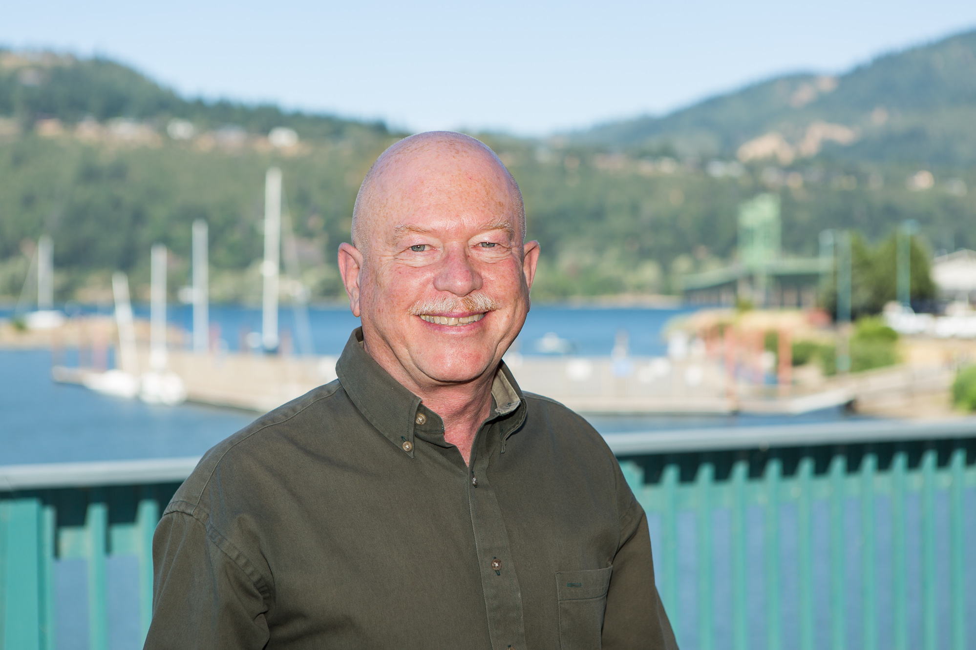 Smiling man with a marina and hills in the background.