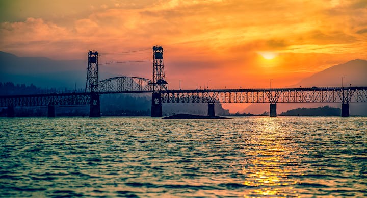 Bridge over water at sunset with mountains in the background.