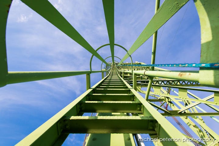 Looking up a green metal ladder structure against a blue sky.