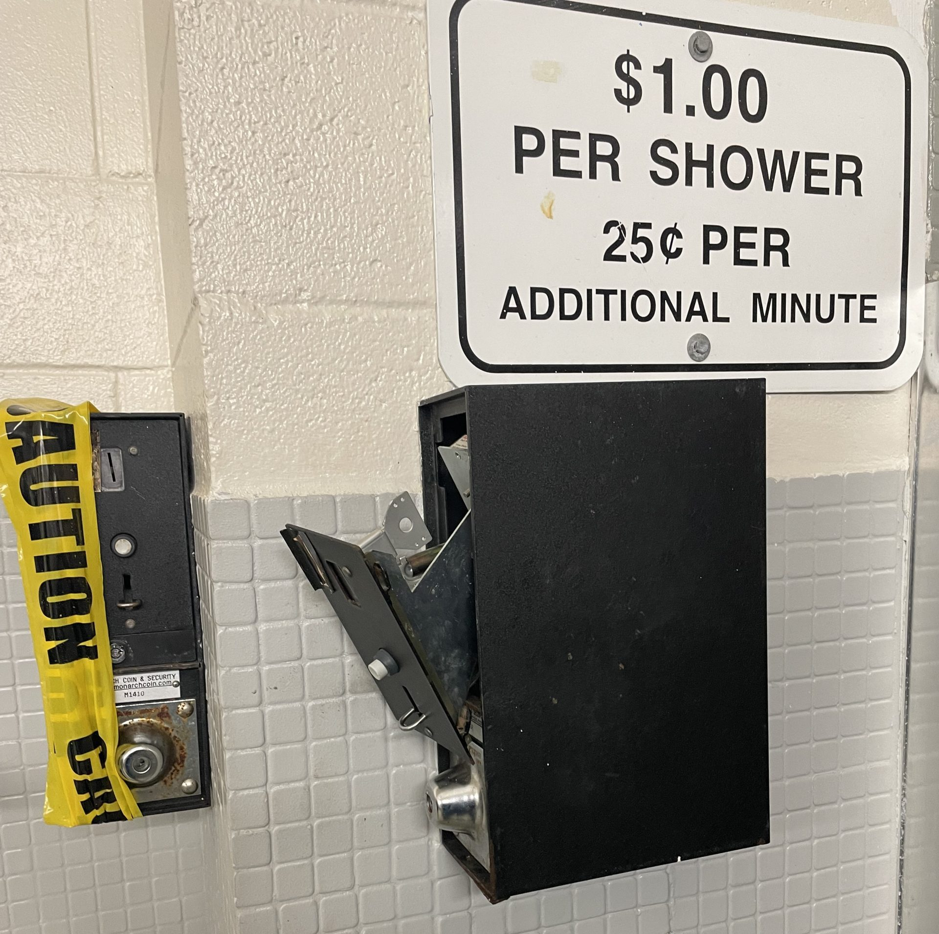 Coin-operated shower timer with pricing sign and caution tape.