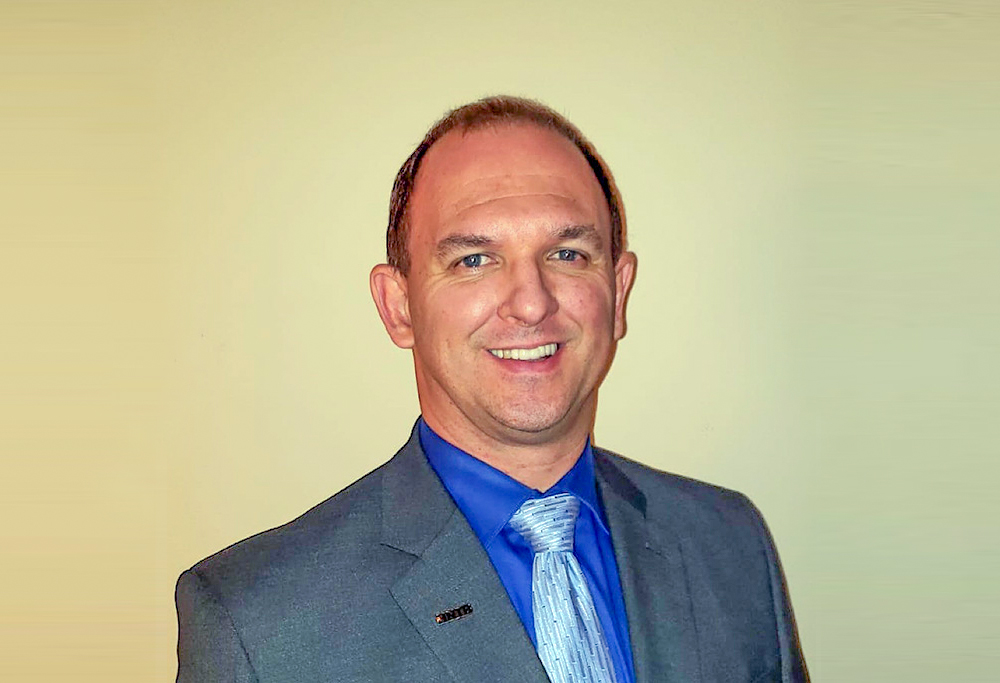 A man in a suit with a blue tie smiling against a light background.