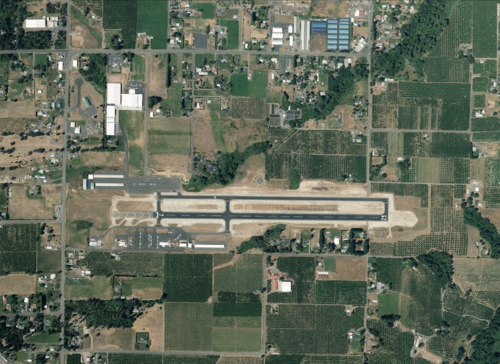 Aerial view of a small airport with a runway, surrounded by farmland and residential areas.