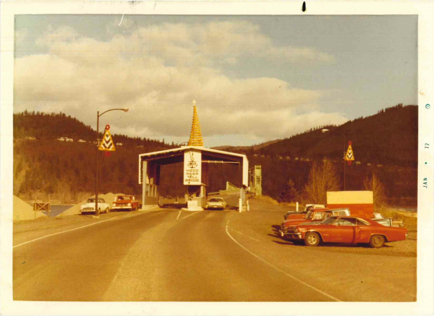 An old photo of a large covered bridge with vintage cars in front, under a clear sky.