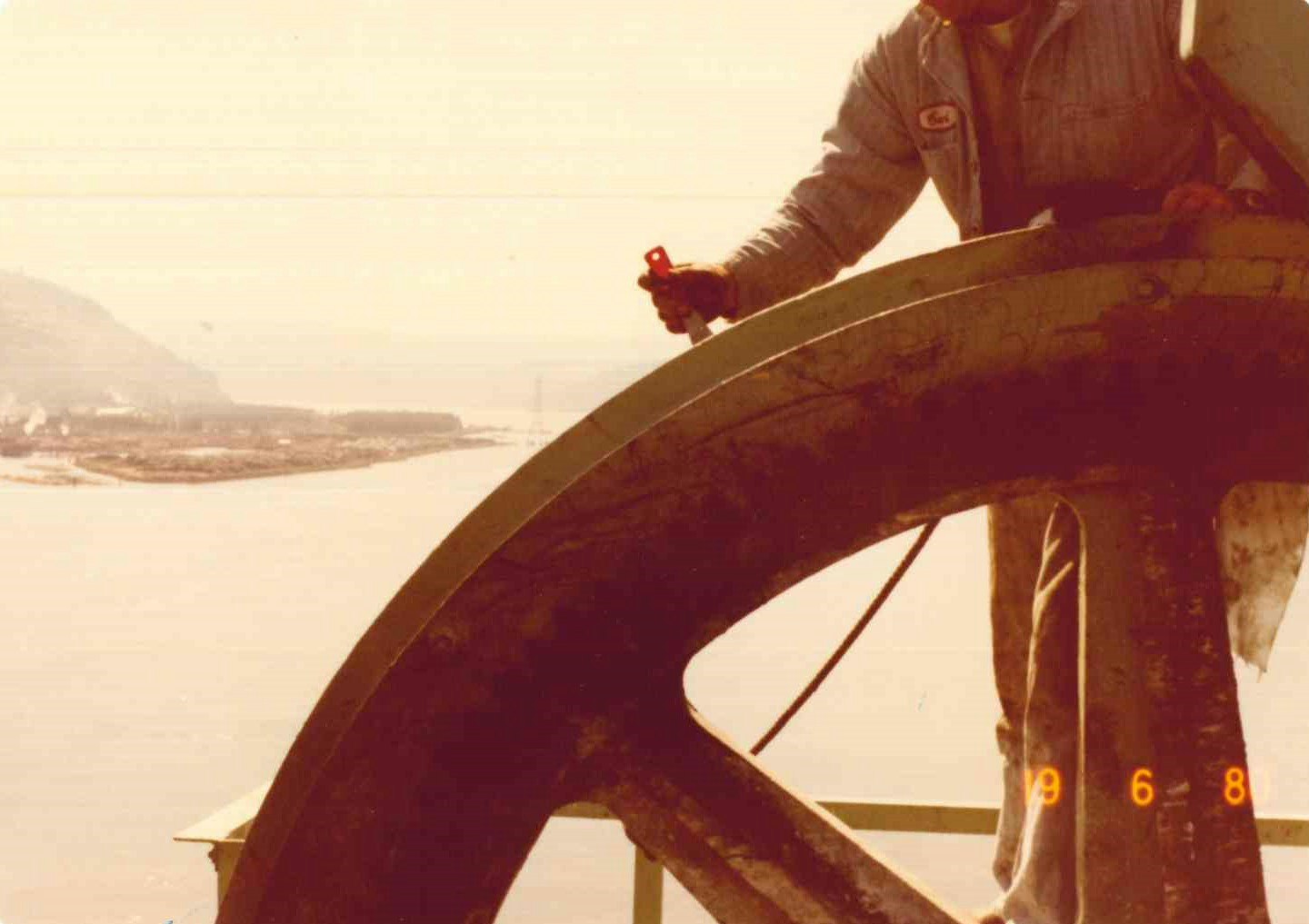 A person's arm holding a small toy by a large wheel, landscape in the background, vintage hues.