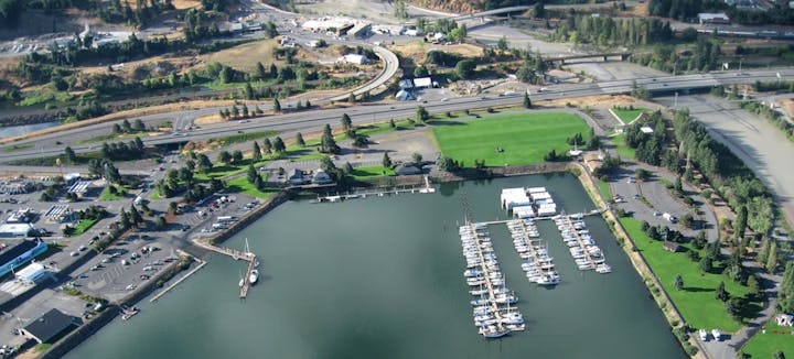 An aerial view of a marina with boats, nearby roads, and green areas, showcasing a mix of urban and natural landscapes.