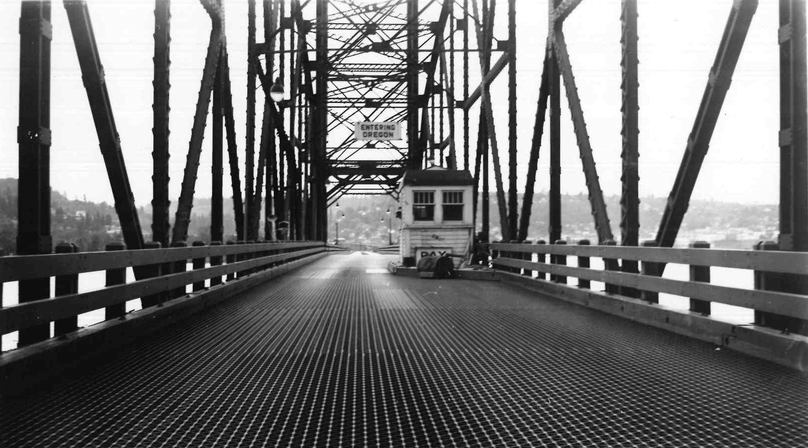 Black and white photo of an old toll booth on a metal truss bridge with "Entering Oregon" sign.