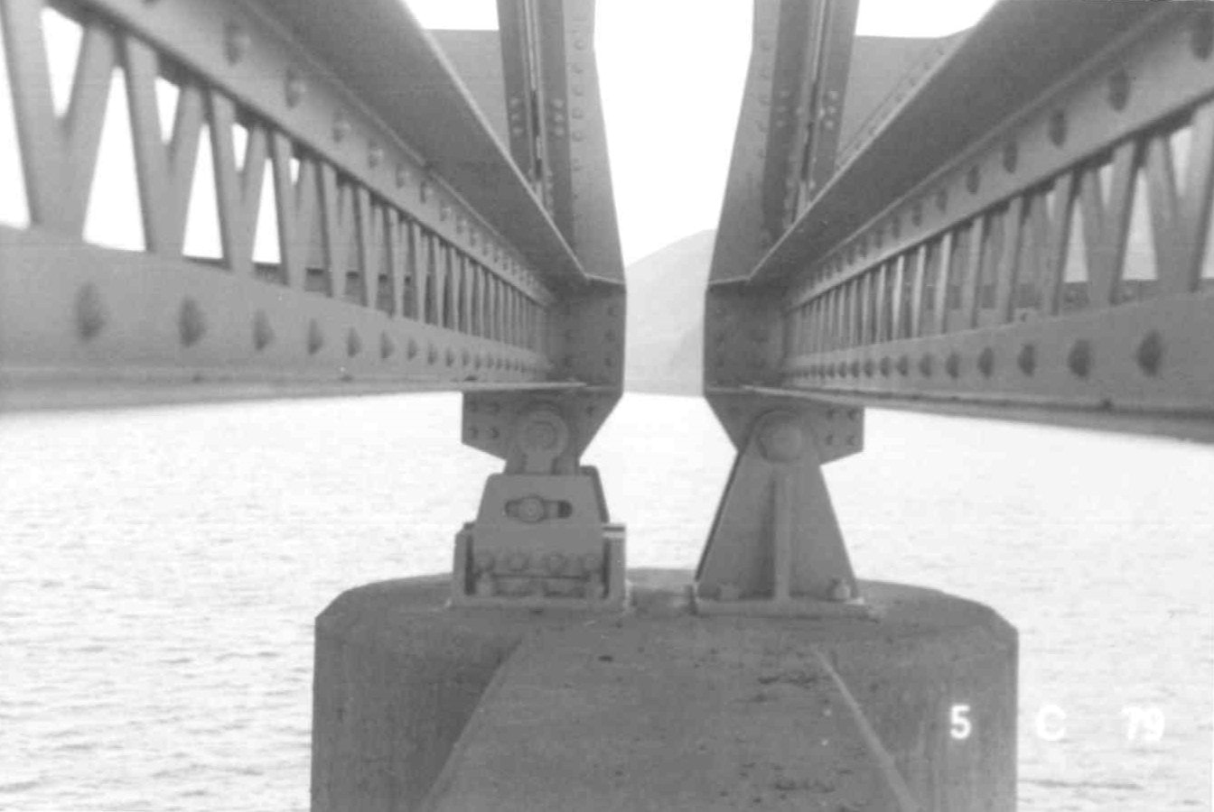 Symmetrical view of a bridge's steel structure with riveted girders and geometric patterns, over water.