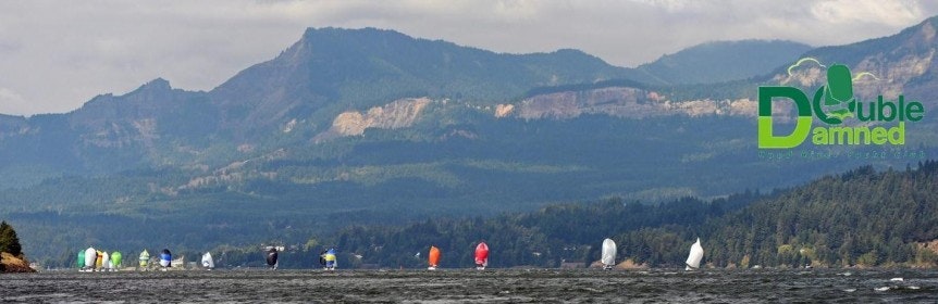 Sailboats with colorful sails on a lake, mountains in the background, and a "Double Damned" logo in the corner.