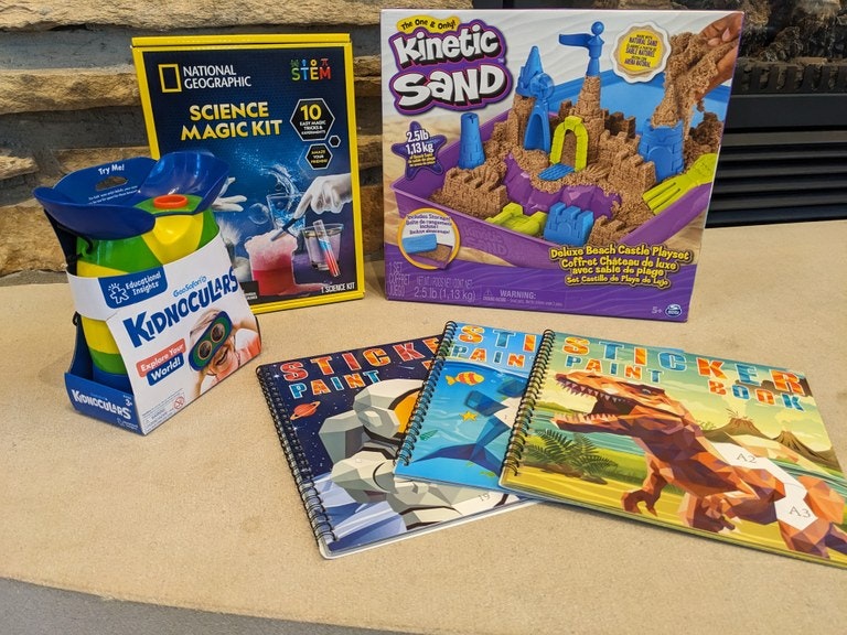 Children's educational and activity items including binoculars, a science magic kit, kinetic sand, and sticker painting books.