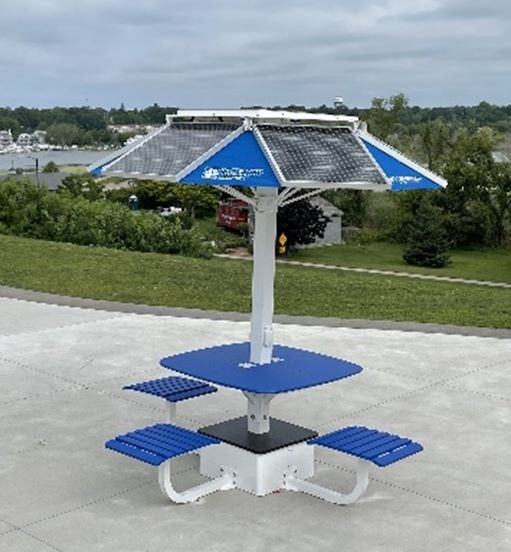 A blue picnic table with a solar panel umbrella, set on a concrete area with a scenic background.