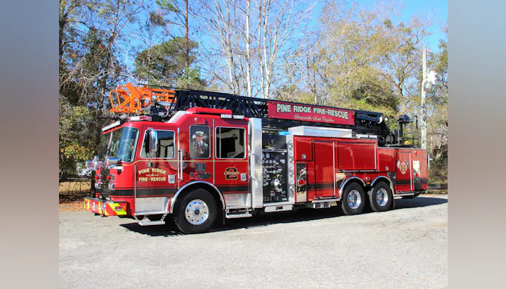 A red fire truck with a ladder, labeled "Pine Ridge Fire-Rescue," parked in a wooded area.