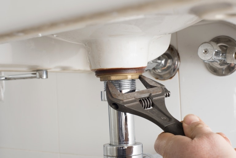 A hand using a wrench to tighten a plumbing fitting under a sink, showing plumbing work in progress.