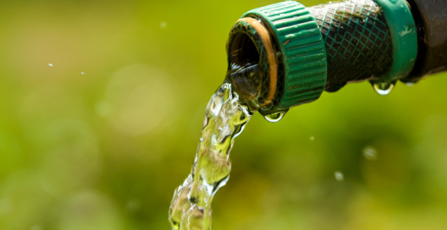 A close-up of a garden hose with water flowing out, set against a blurred green background.