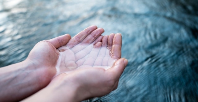 A pair of hands cupping clear water, reflecting tranquility against a blurred watery background.