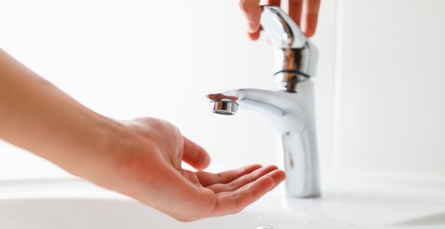 A hand is reaching out to catch water from a modern faucet in a bathroom setting.