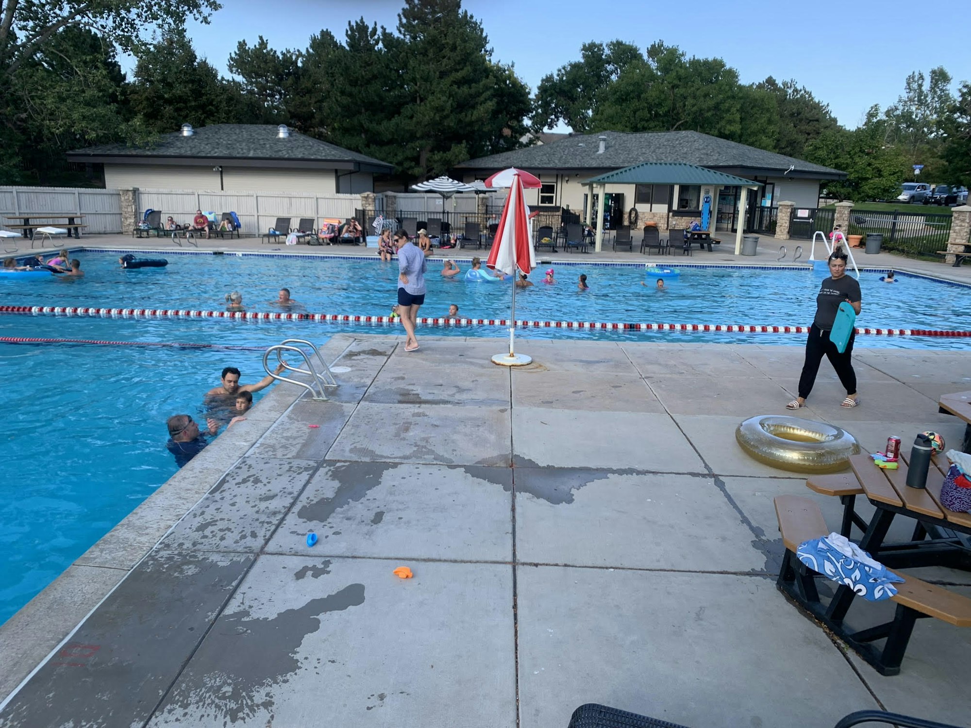 People swimming and relaxing at an outdoor pool with tables and chairs nearby.