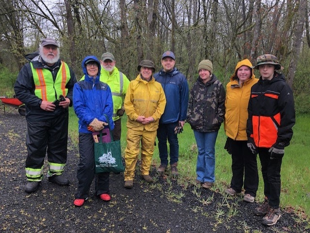A group of people outdoors in rain gear, standing on a gravel path with trees in the background.