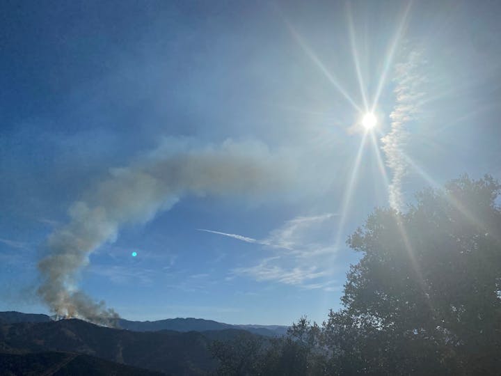 Sunshine, blue sky, smoke plume from hill, lens flare.