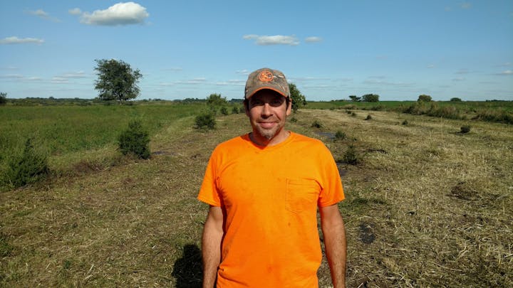 May contain: clothing, t-shirt, face, head, person, photography, portrait, soil, field, grassland, nature, outdoors, wilderness, grass, plant, hat, vegetation, land, sky, cap, tree, adult, male, man, and baseball cap