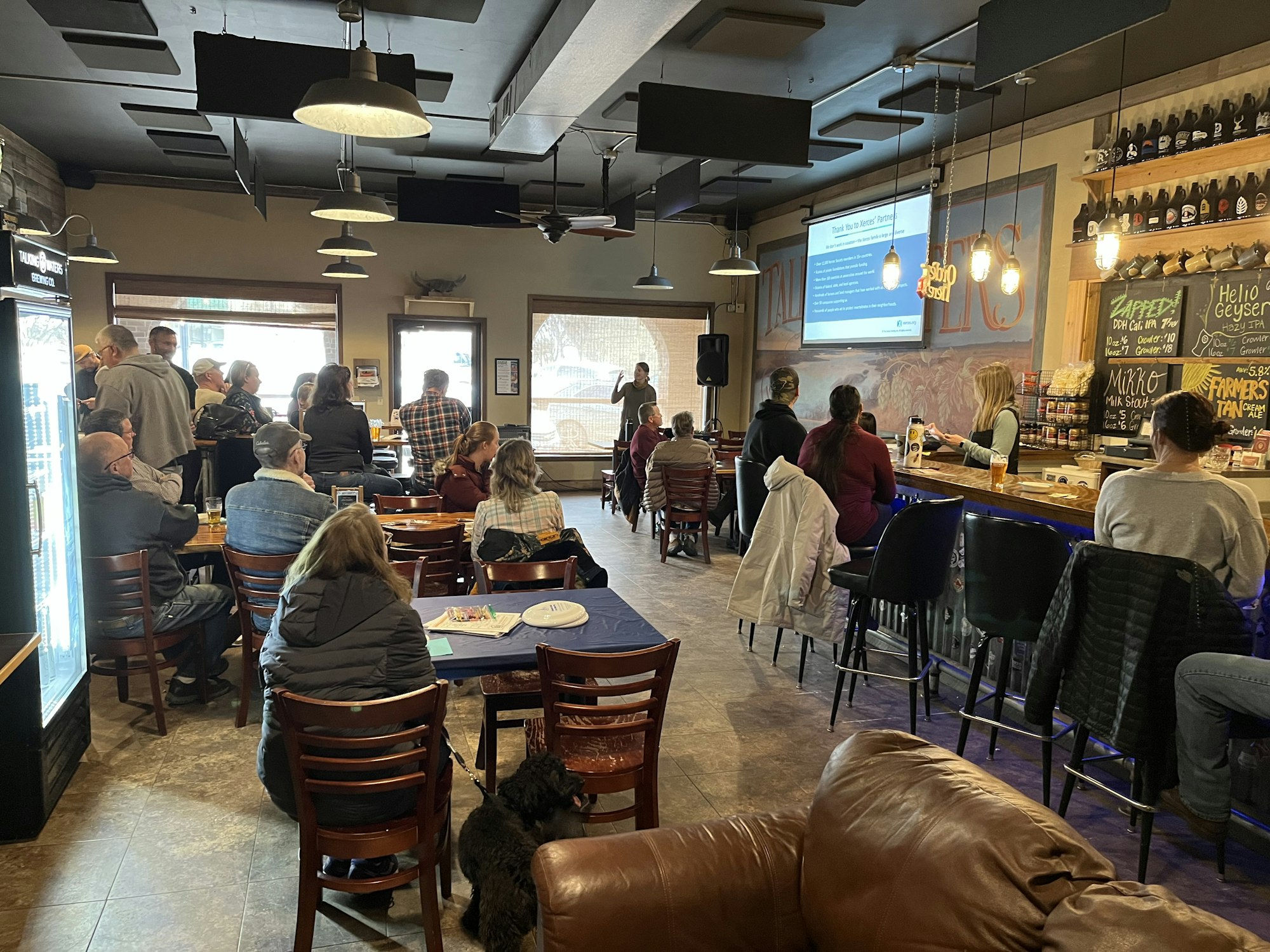 People gathered in a bar or cafe watching a presentation on a screen.