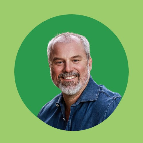 A smiling man with a beard, in a blue shirt, against a green circle backdrop.