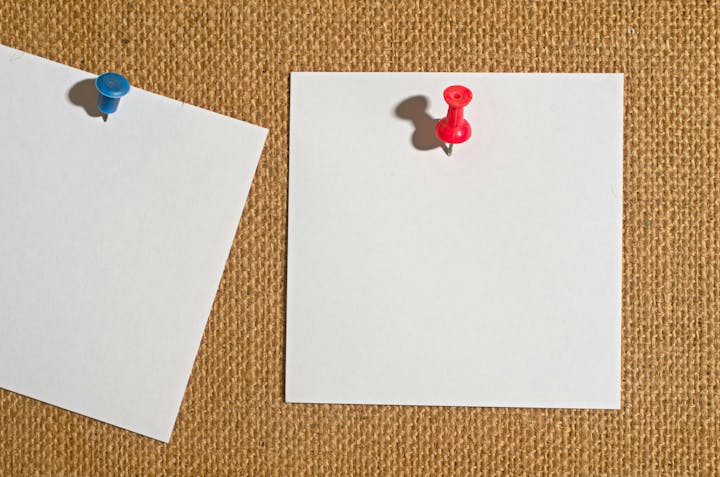 Two pushpins on blank white papers against a burlap background.