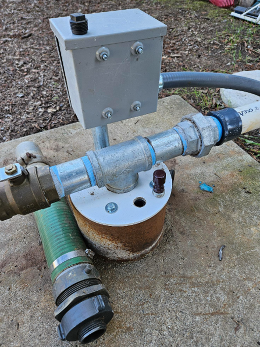 A metal pipe assembly with connected hoses and a junction box, possibly part of a water or fluid system.