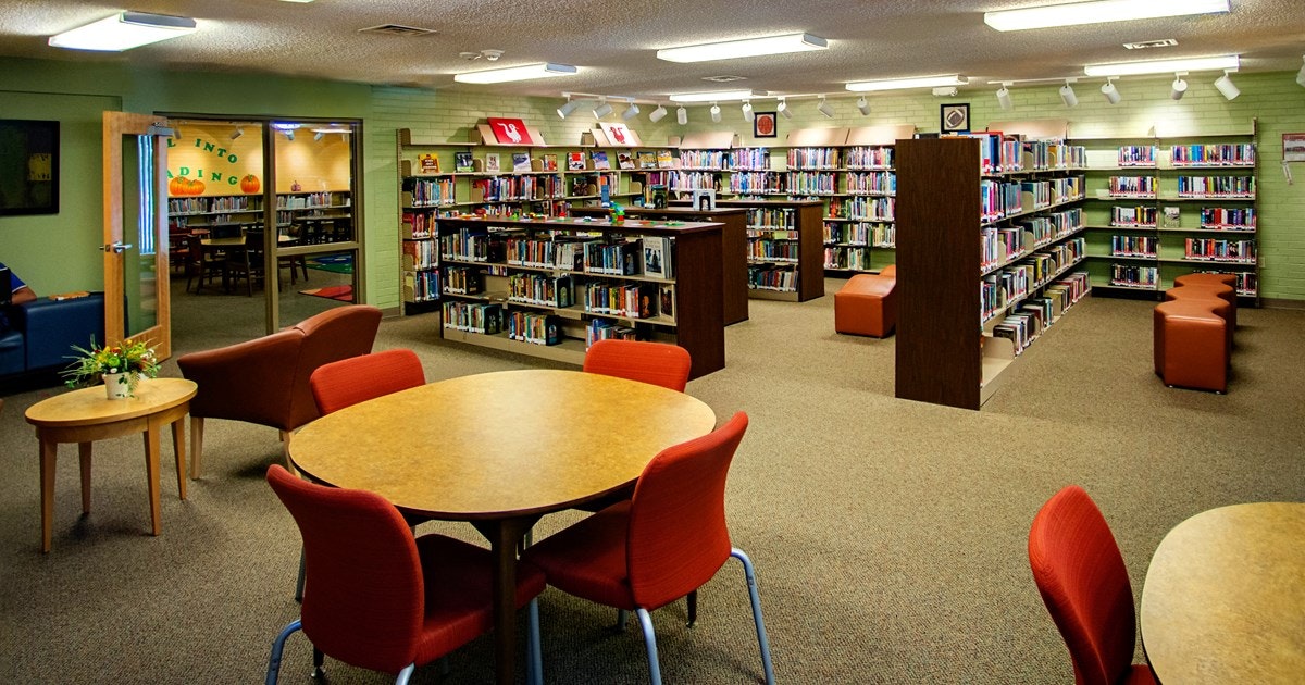 A cozy library with bookshelves, tables, chairs, and a sitting area.