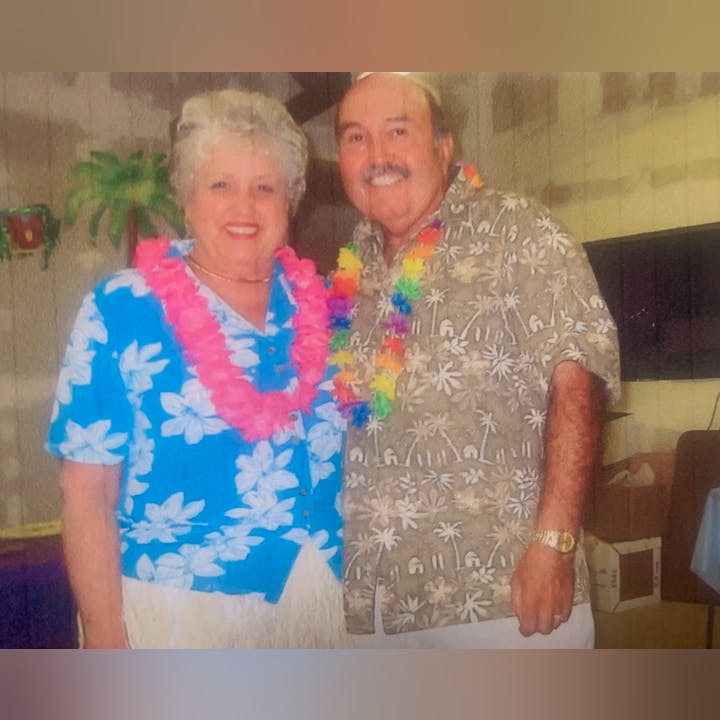 Two people wearing tropical-themed shirts and leis, standing indoors.