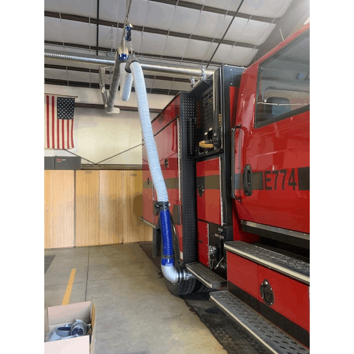 Red fire truck inside a station, with exhaust hose attached.