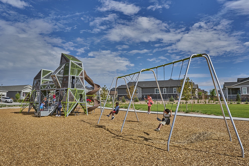 Kids playing on swings and climbing equipment in a playground under a blue sky.