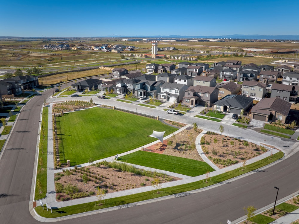 Suburban neighborhood with houses, roads, and a central grassy park area with a white canopy.