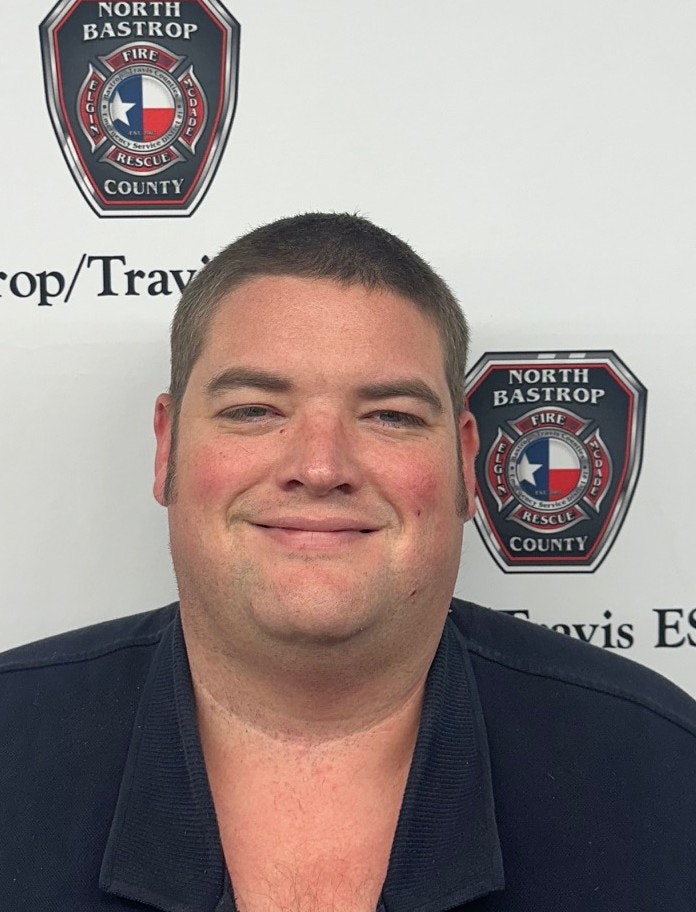 The image features a man smiling against a background with fire department logos from North Bastrop County.