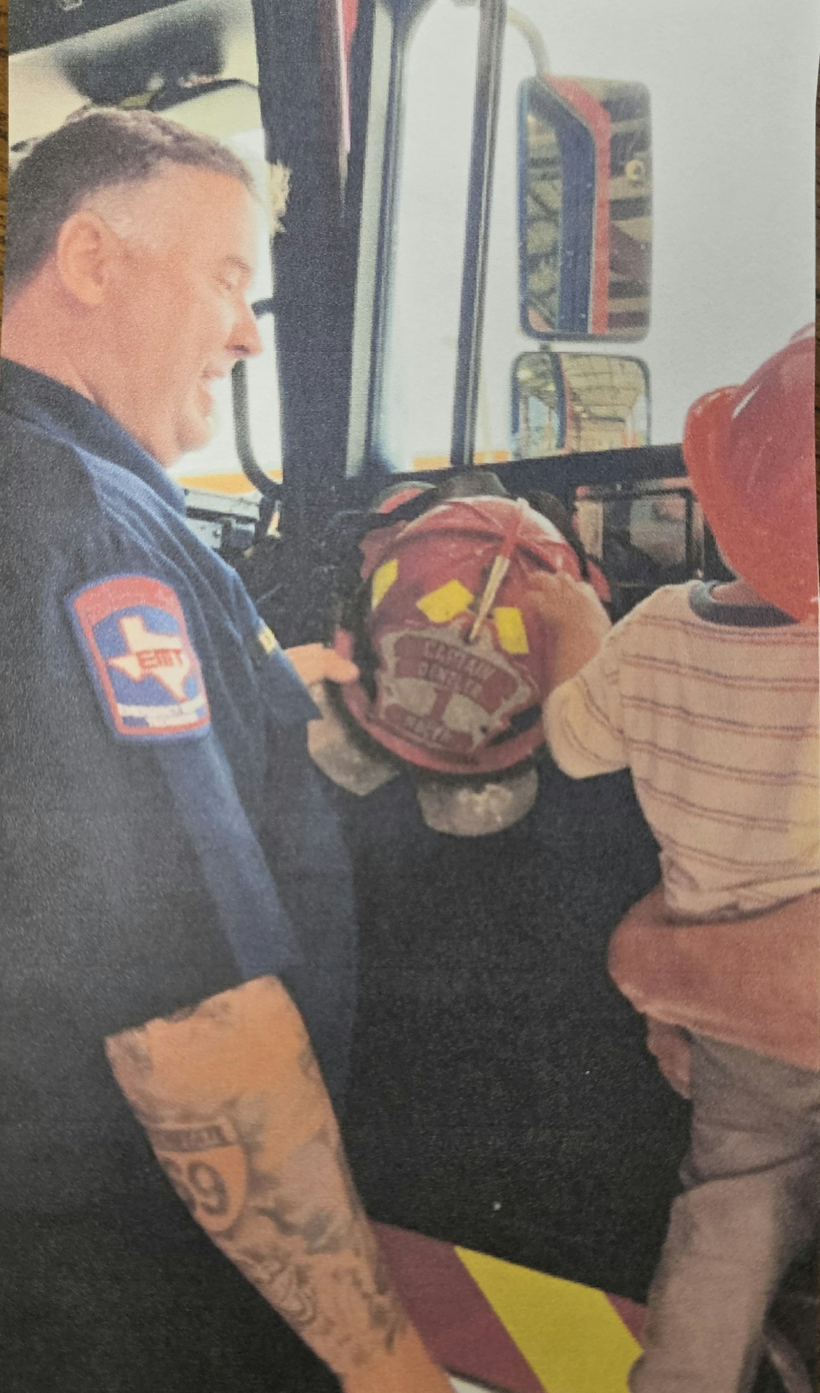 A firefighter with a child in a fire truck, holding a firefighting helmet.