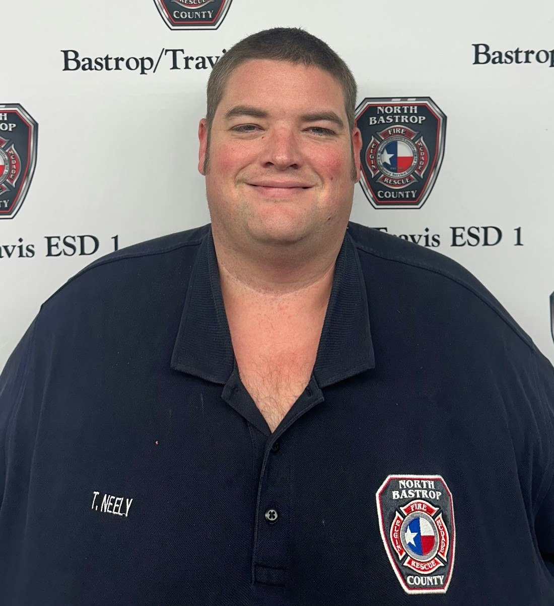 A person in a North Bastrop Fire Rescue uniform standing in front of a backdrop with text and logos.