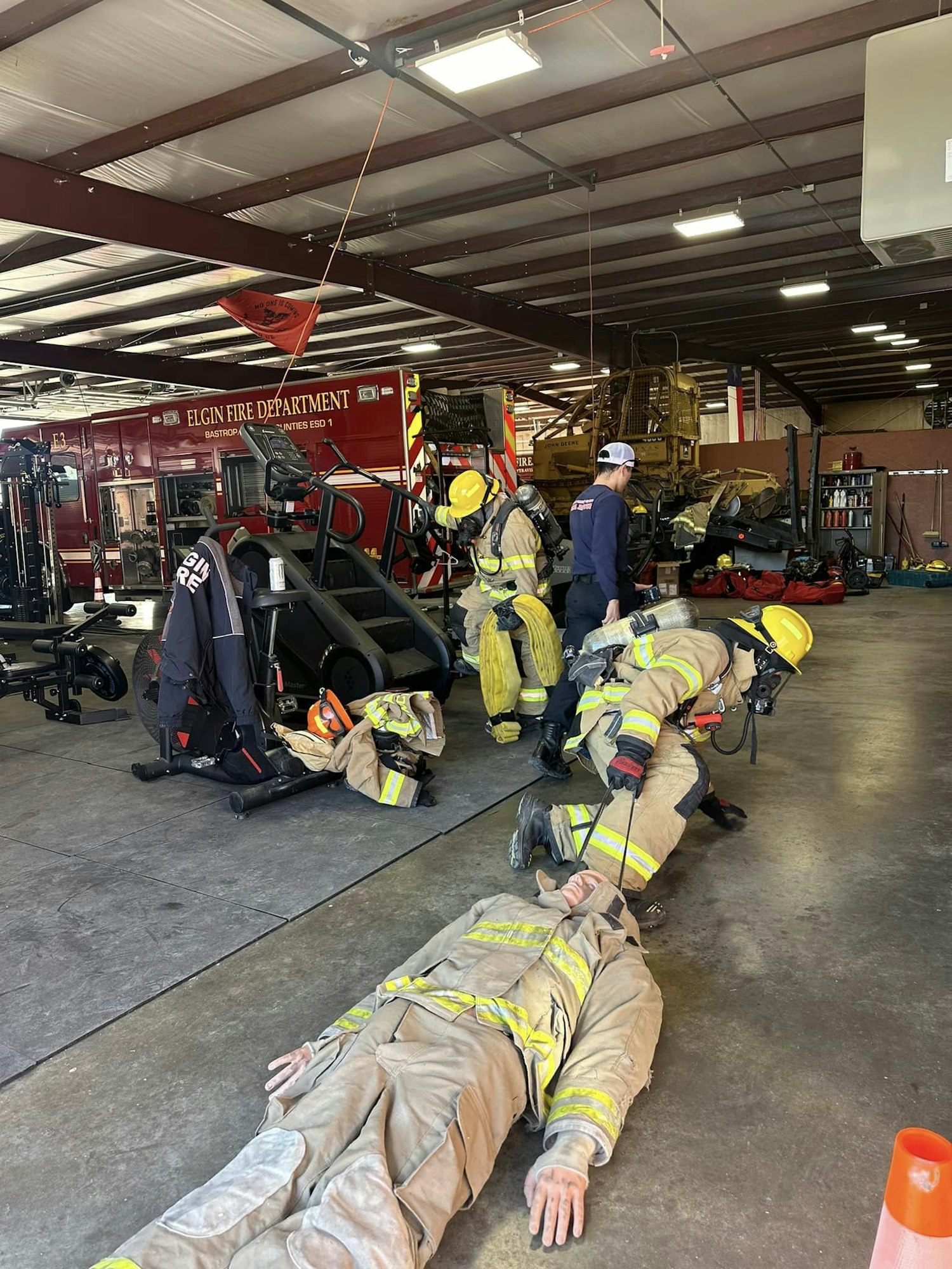 Firefighters in gear at a fire station with a firetruck in the background.