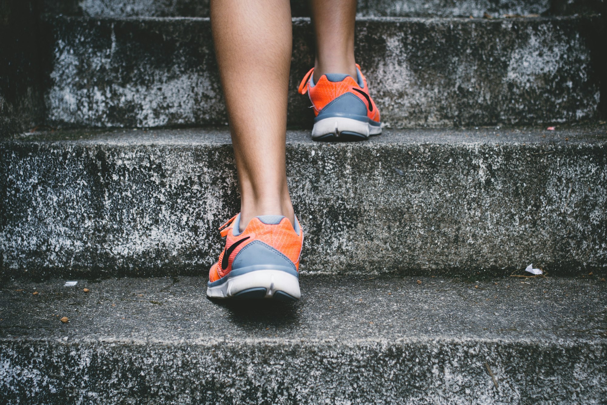 A person is ascending stone steps while wearing bright orange and gray sneakers.