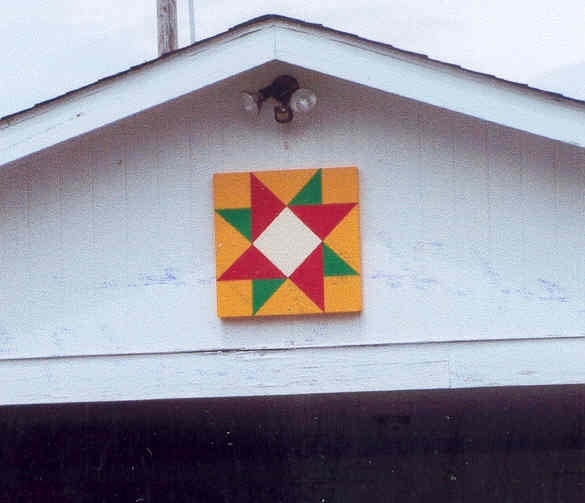A barn quilt with a colorful star pattern mounted on the exterior of a building's gable.