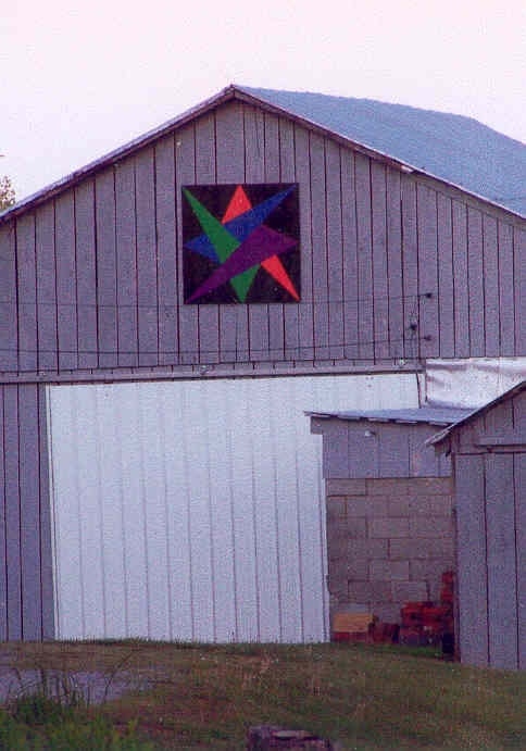 A barn with a colorful quilt pattern design on its upper section.
