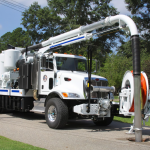 A vacuum truck with a long hose used for cleaning/waste removal services.