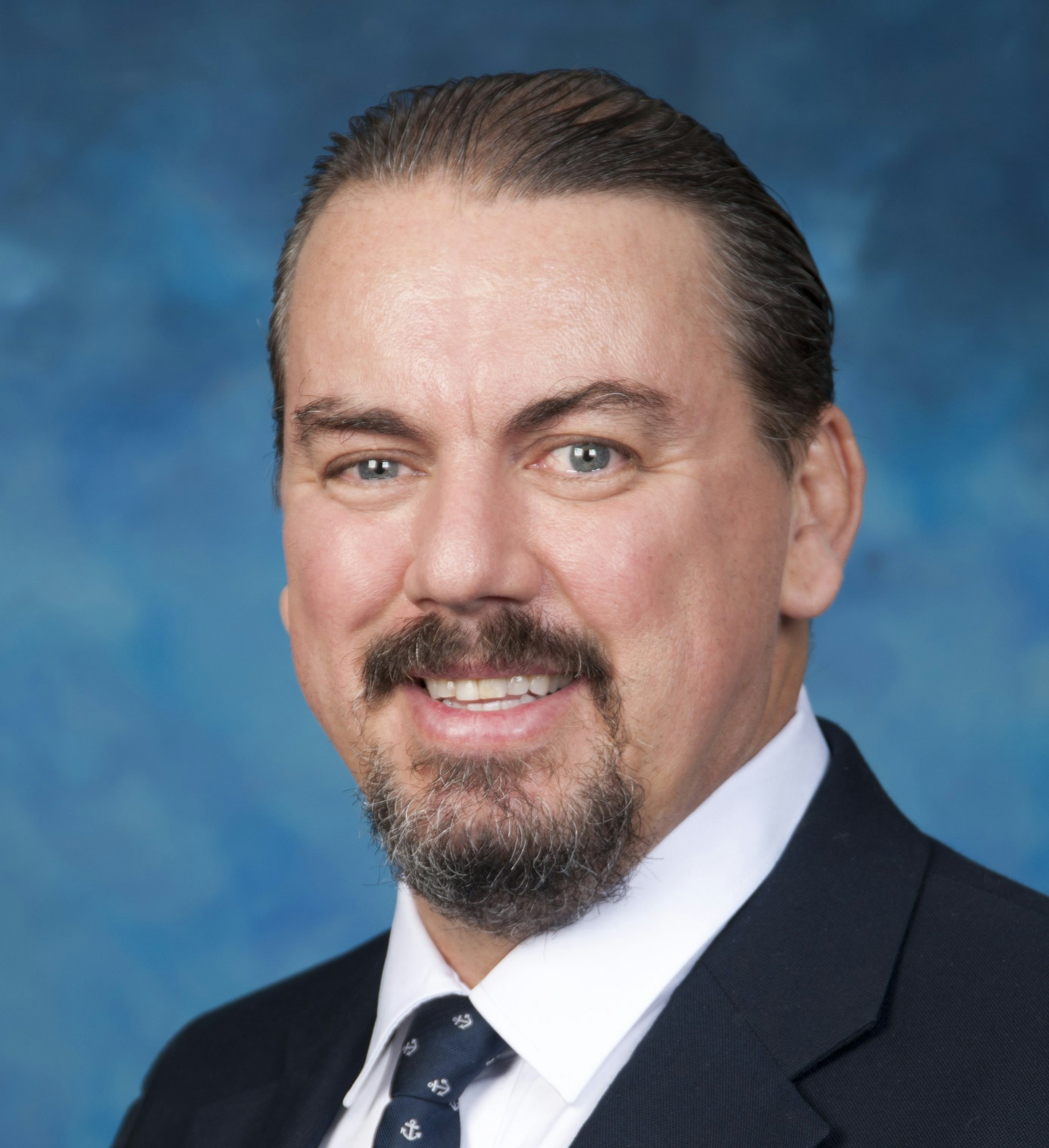 A man with a beard, mustache, and suit against a blue background.