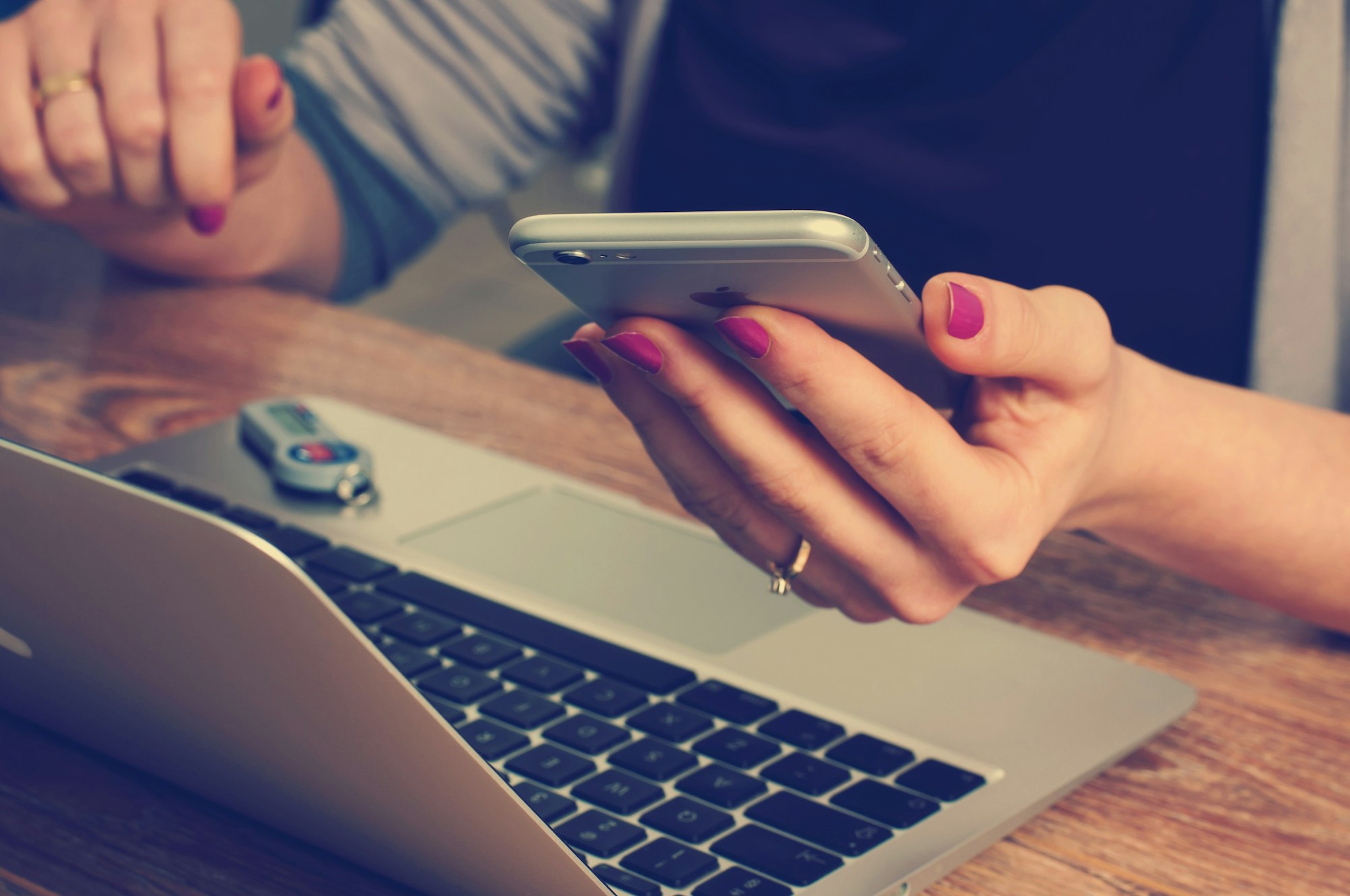Person holding a smartphone with a laptop and USB drive on a wooden table.