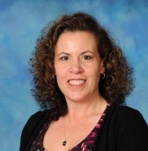 A woman with curly hair, smiling, wearing a black cardigan and patterned top, against a blue background.