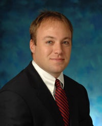 A man in a suit with a red tie on a blue speckled background.