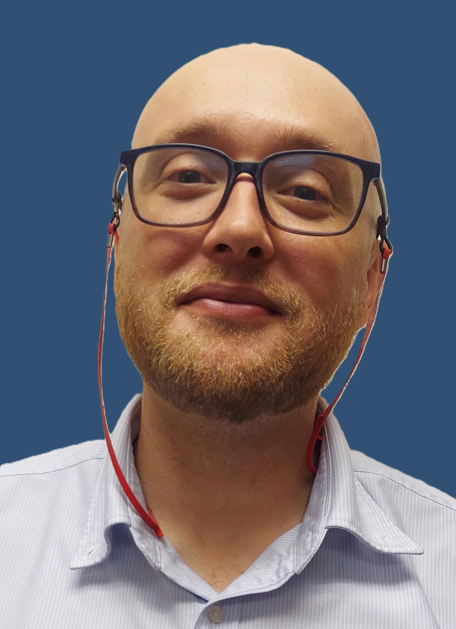 A smiling person with glasses and a short beard, wearing headphones, against a solid blue background.