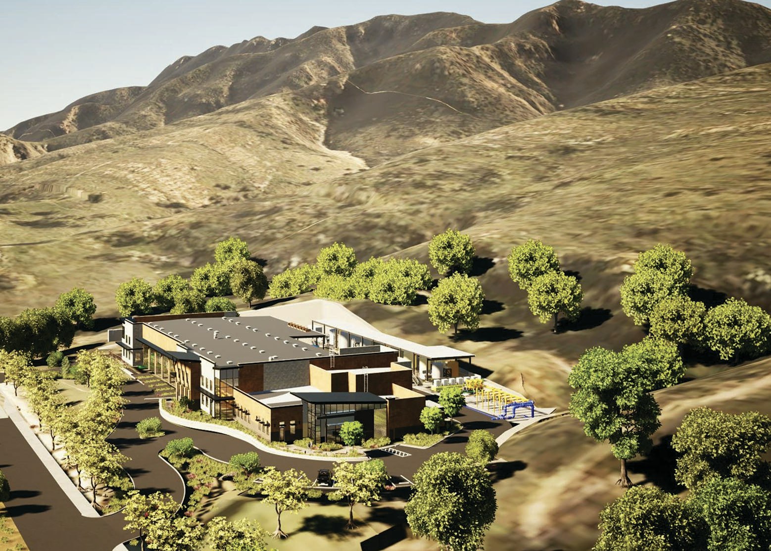 Aerial view of a modern building surrounded by trees, set against a backdrop of hills and mountains.